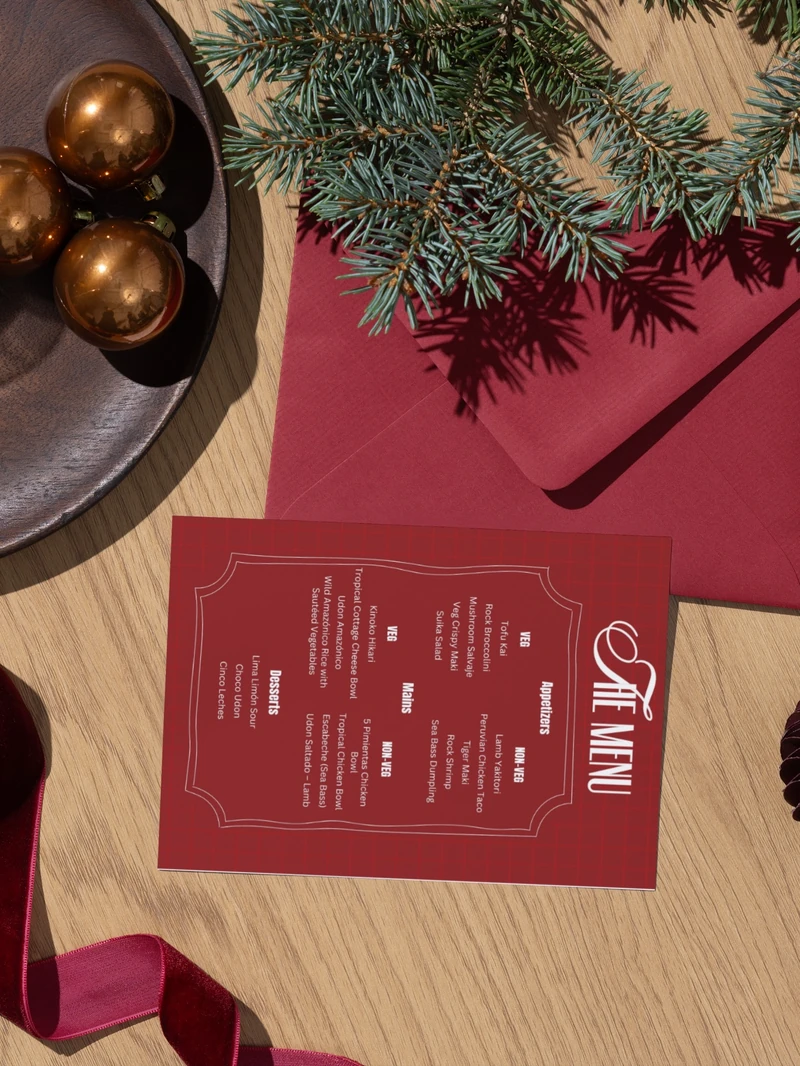 Photograph of the red menu in a festive place setting with evergreen branches, ornaments and ribbon.